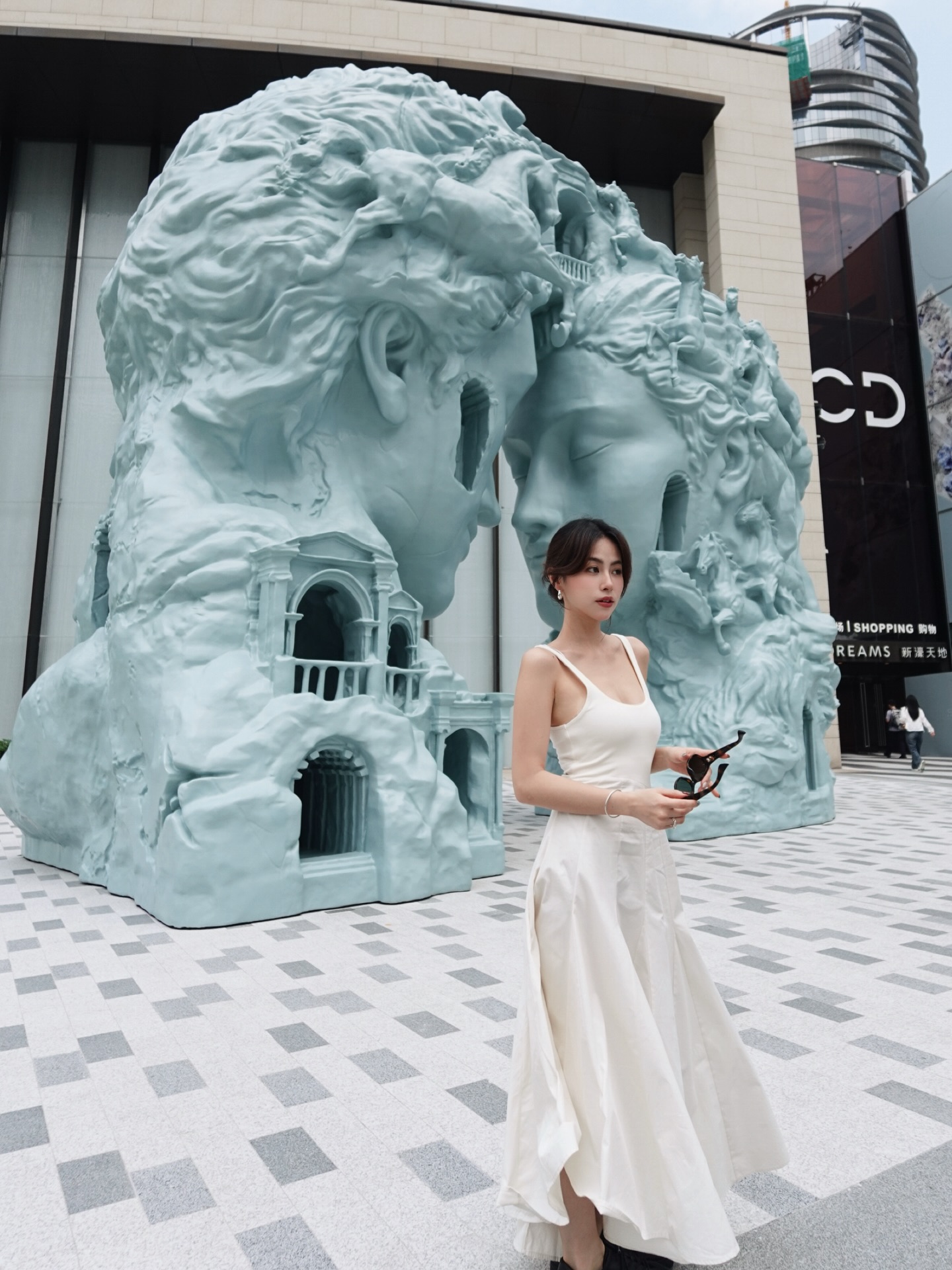 白色露背长裙，剪裁简约却气质满分，在艺术雕塑前文艺感溢出屏幕