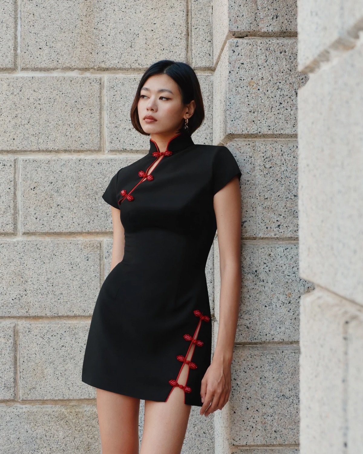 新中式改良旗袍，立领红色盘扣+黑色裙身，短发干练配石墙背景，清冷高级感