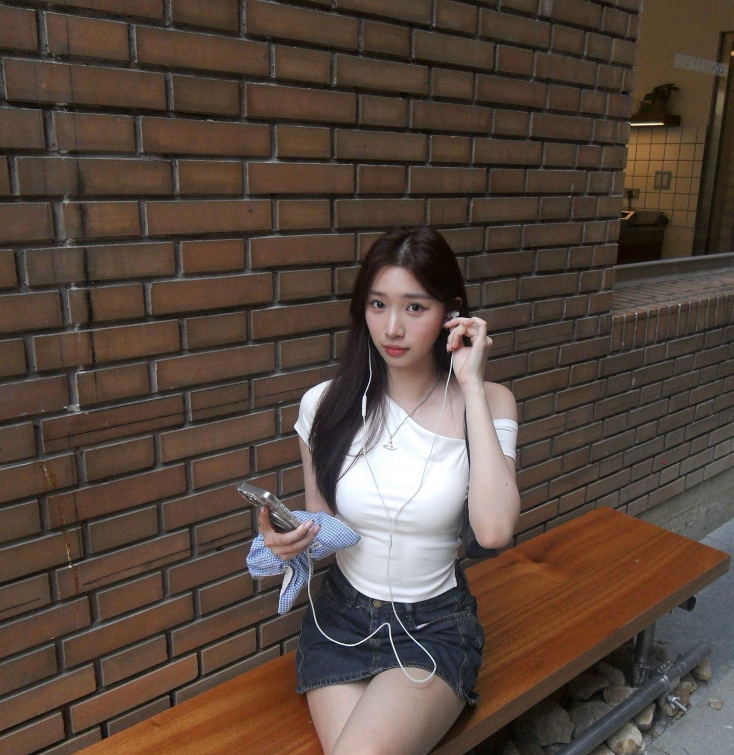 白色斜肩上衣+深色牛仔短裙，Y2K星球项链点睛，红砖墙前的青春时髦感