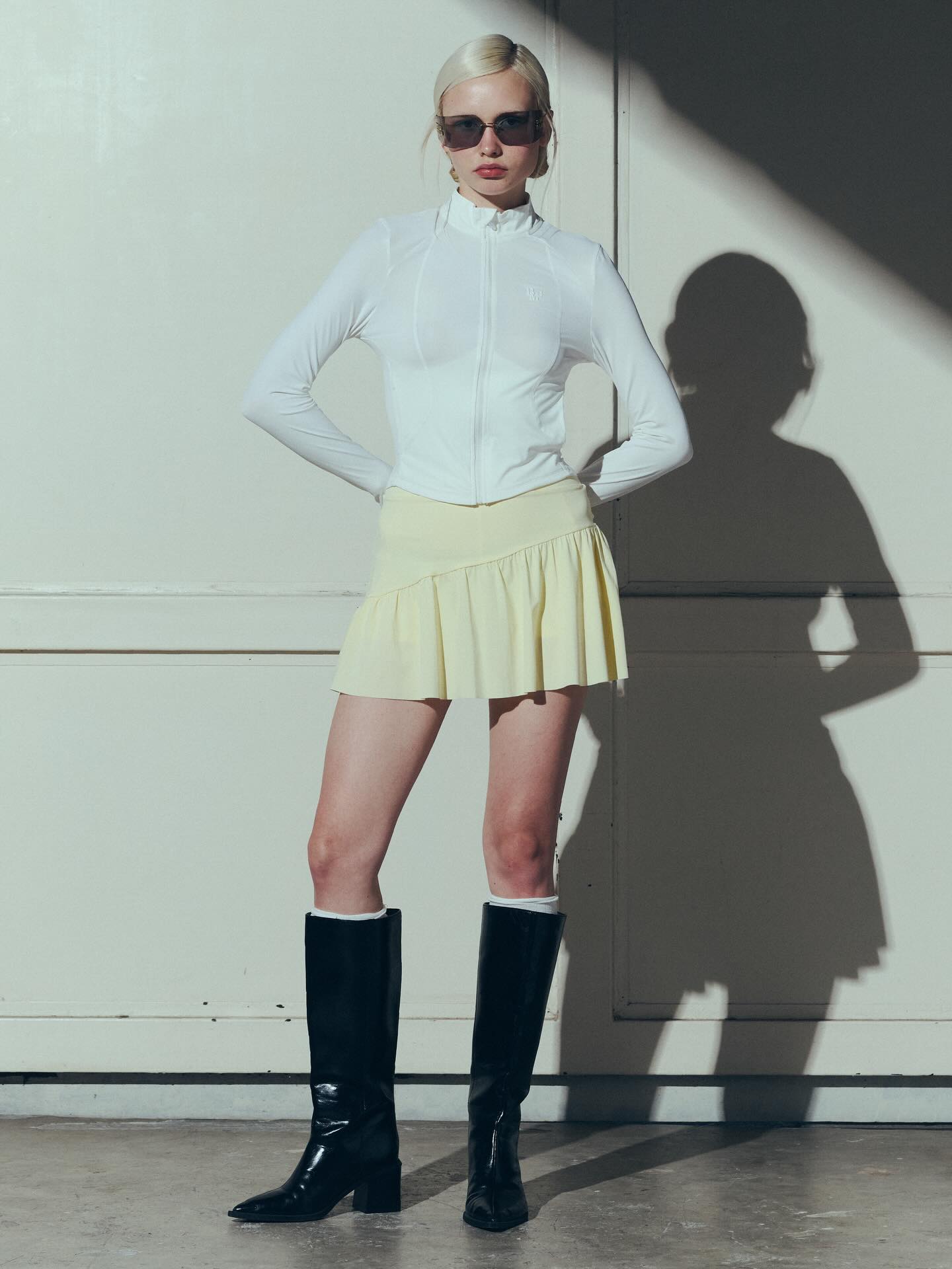 白色紧身运动外套+淡黄色百褶短裙，黑色长筒靴，光影硬朗气场干练高级的极简运动风