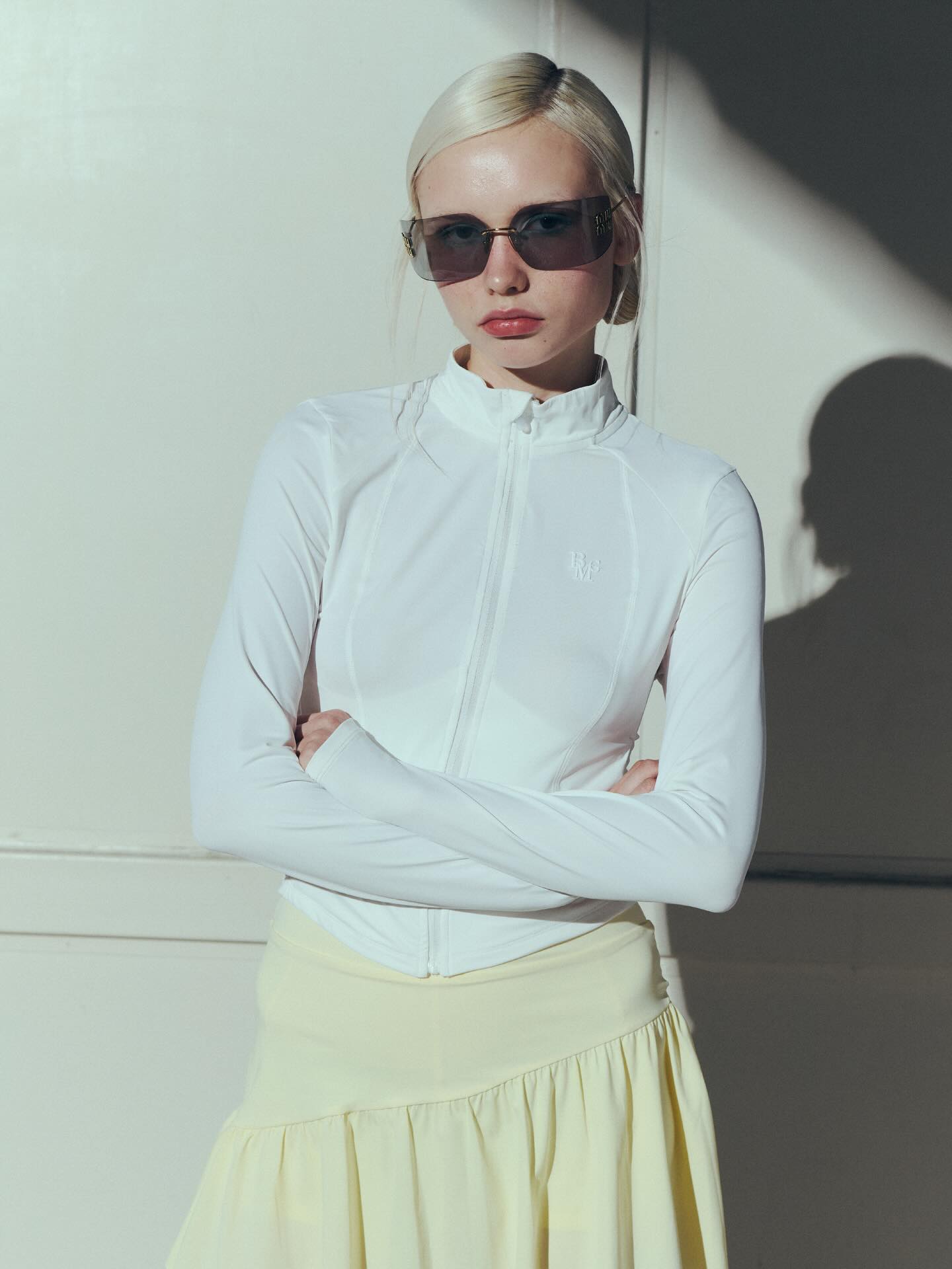 白色紧身拉链运动上衣+淡黄色百褶长裙，混搭科技感与柔美，白金发色疏离前卫杂志感