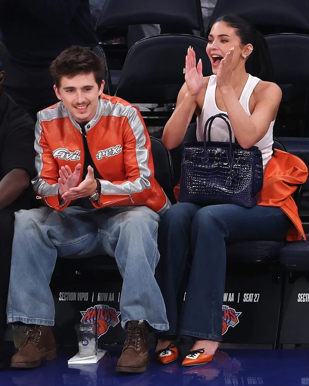 Timothée Chalamet橙银赛车夹克配Kylie Jenner白色背心，NBA情侣场边穿搭
